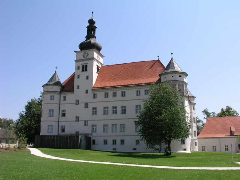 Foto vom Gebäude Schloss Hartheim von vorne, auf der Seite ein Baum.