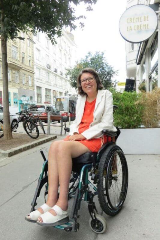 Expertin Maria Grundner legt Wert auf Barrierefreiheit Expertin Maria Grundner trägt ein orangenes Kleid mit weißem Blazer und sitz in einem Rollstuhl.