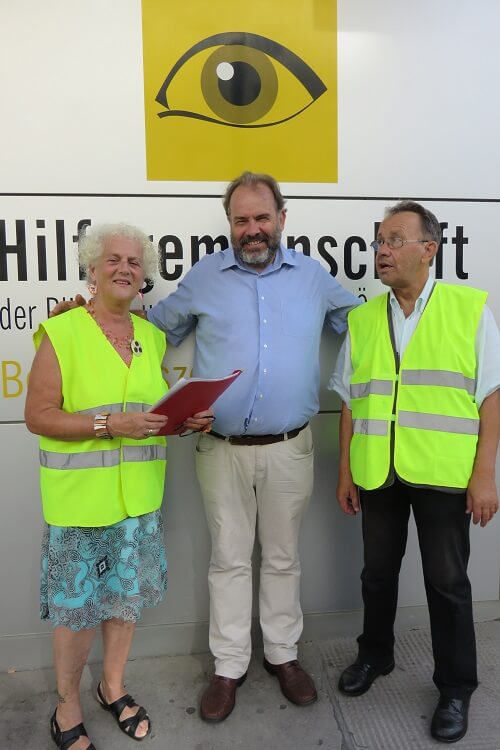 Hubert Wagner (Mitte) mit „Ampelpaten“ Veronika Kerschbaum und Michael Watz Hubert Wagner posiert mit „Ampelpaten“ Veronika Kerschbaum und Michael Watz lächelnd für ein Foto vor dem Eingang der Hilfsgemeinschaft.