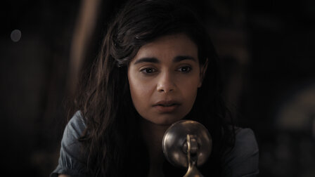 Unser Netflix-Filmtipp: Aria Mia Loberti als blinde junge Frau in "All The Light We Cannot See". Foto: Netflix. Junge Frau mit dunklen langen Haaren spricht in ein Mikrofon