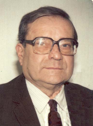 Ein Herr mittleren Alters mit großer Brille, Anzug und Krawatte blickt leicht lächelnd in die Kamera