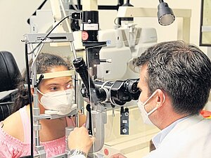 Gian bei einer Routineuntersuchung mit Netzhautspezialist Markus Ritter im Wiener AKH: „Die Gentherapie erhöht die Lebensqualität deutlich“. Arzt schaut durch Linse das Auge eines Mädchens an