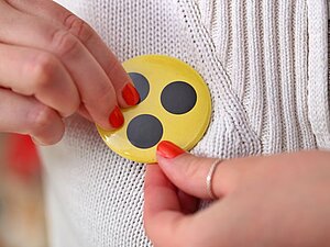 Gelber Button mit drei schwarzen Punkten