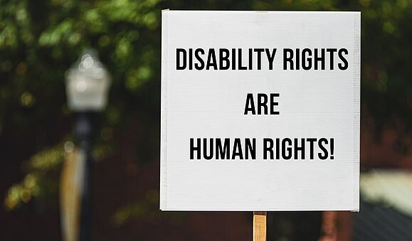 Klaus Höckner und Daniele Marano begleiten die Delegation des Österreichischen Behindertenrates zur Staatenprüfung der UN in Genf. Protestschild vor Baum: "DISABILITY RIGHTS ARE HUMAN RIGHTS!"