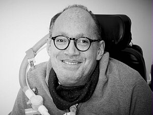 Mann mit Brille sitzt lächelnd im Rollstuhl
