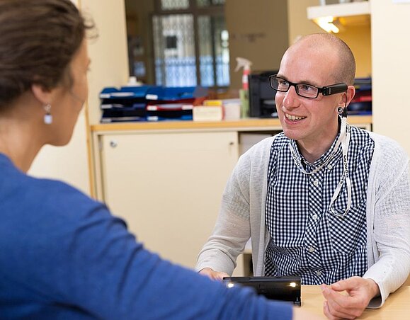 Wegweiser_Freiwilligenarbeit-Das_Freiwilligen_Erstgespraech__c_Schedl_Hilfsgemeinschaft_A5.jpg Frau von hinten quatscht mit Herrn mit Glatze und Brille in kariertem Hemd