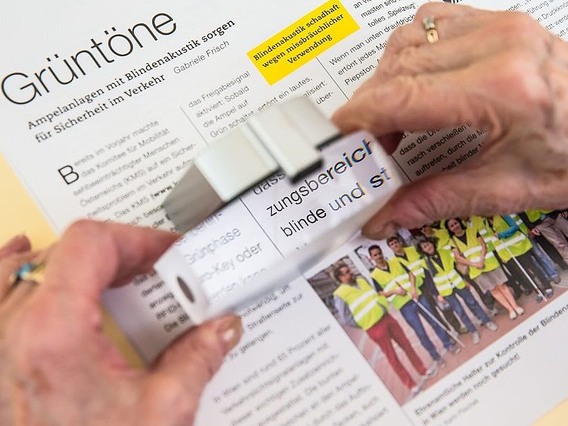 Über einem Artikel aus einem Magazin wird eine rechteckige Lupe mit zwei Händen gehalten.