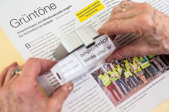 Lesen mit Lupe, Copyright: Franz Pfluegl Über einem Artikel aus einem Magazin wird eine rechteckige Lupe mit zwei Händen gehalten.