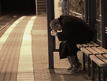 Ein verzweifelter Mann sitzt traurig und einsam an einer Haltestelle.