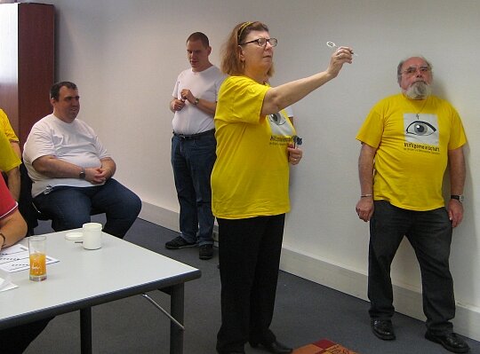 Die Darts-Gruppe der Hilfsgemeinschaft lud die Freunde aus Budapest zu einem Vergleichsturnier ein. Eine blinde Frau zielt mit einem Dartpfeil auf eine Scheibe, ein Mann sieht ihr dabei zu, zwei Männer stehen und sitzen hinter ihr.