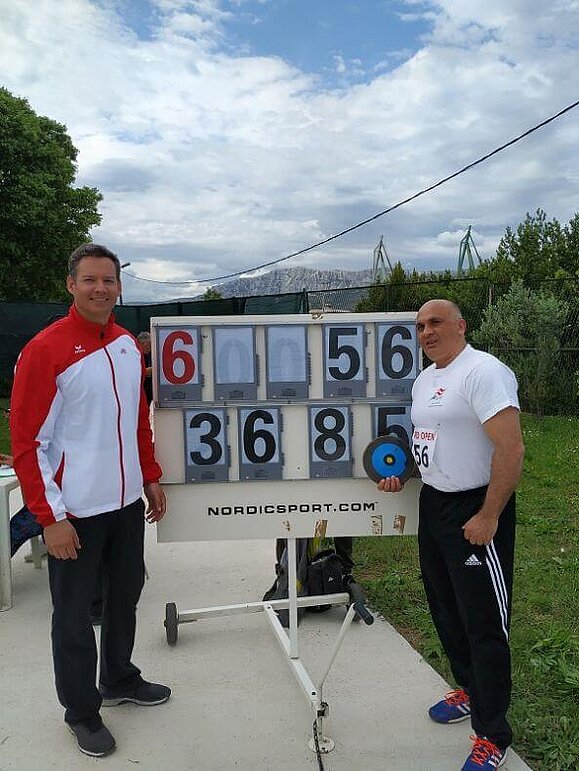 Gerhard Mayer und Bil Marinkovic bei den Croatia Open Athletics, Copyright: Gerhard Mayer Zwei Männer stehen vor einer Punktetafel. Marinkovic hält einen Diskus in seiner rechten Hand.