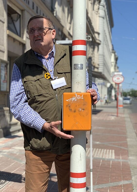 Mann mit Kennzeichnung und Langstock drückt die Akustikampel