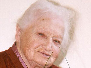 Stefanie Fleischmann Eine ältere Dame lächelt in die Kamera, vor ihr ist ein großer Blumenstraß zu sehen.