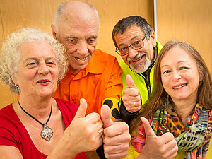 Zwei Damen und zwei Herren bilden eine Gruppe und halten lächelnd ihre Daumen in die Höhe