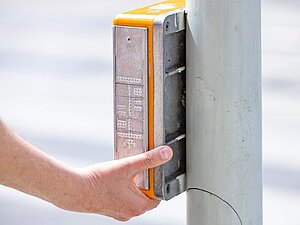 Hand drückt Akustische Ampel mit taktiler Topografie der Kreuzung drauf