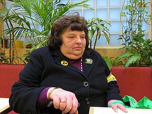 Frau Jolic war sehr verzweifelt als sie zu uns in die Beratung kam. Foto: Eine blinde Frau sitzt auf einem roten Sofa und guckt traurig