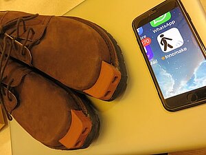 Braune Herrenschnürrschuhe mit Applikation vorne, daneben ein Smartphone mit der App Innomake.