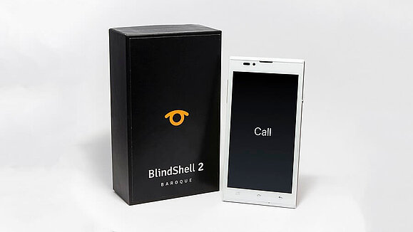 Smartphone BlindShell für blinde und sehbehinderte Benutzer, Copyright: BlindShell. Weißes Smartphone mit großem Display, daneben die schwarze Verpackung des Smartphones, Copyright: BlindShell.