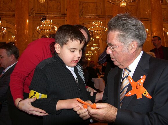 Kind mit gelber Armbinde gibt altem Mann die Hand