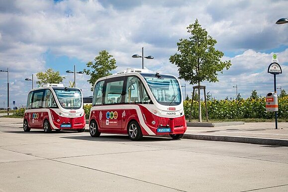 Autonome Busse in der Seestadt Aspern, Copyright: Wiener Linien/Manfred Helmer Zwei Rot-weiße E-Busse stehen im Freien, im Hintergrund der Himmel und Bäume