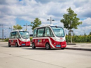 Zwei Rot-weiße E-Busse stehen im Freien, im Hintergrund der Himmel und Bäume