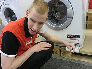 Junger Mann hockt vor Waschmaschine