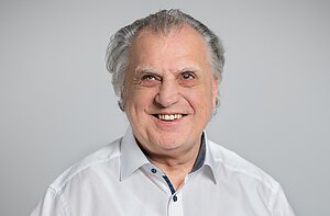 Foto von einem Mann mit weißen Haaren der in eine Kamera lächelt