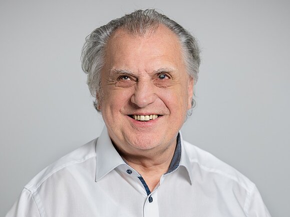 Foto von einem Mann mit weißen Haaren der in eine Kamera lächelt