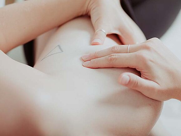 Eine Frau tastet im Liegen ihre Brust ab, Nahaufnahme.