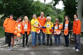Gemeinsam für den guten Zweck - World Vision Österreich und die Hilfsgemeinschaft eröffnen den Global 6K in Österreich, Copyright: World Vision Österreich. 9 Personen in orangen und gelben Shirt hinter der Startlinie der Wanderung, Copyright: World Vision Österreich.