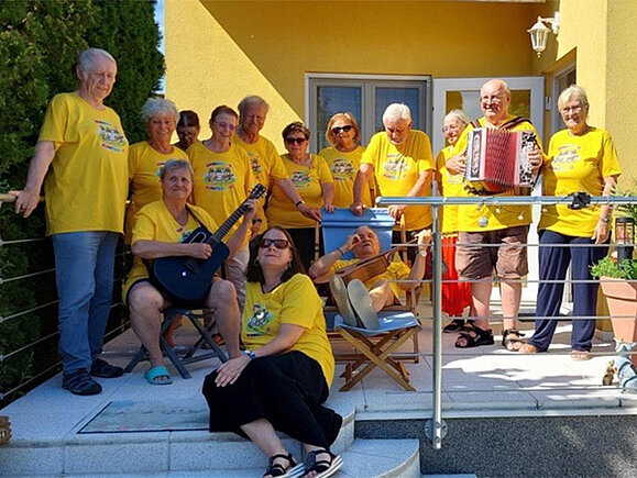 Die Mitglieder der Singgruppe Kunterbunt, teils mit Instrumenten auf der Terrasse eines Hauses.
