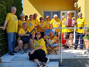 Die Singgruppe Kunterbunt trifft sich alle zwei Wochen. Die Mitglieder der Singgruppe Kunterbunt, teils mit Instrumenten auf der Terrasse eines Hauses.