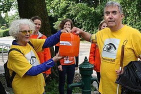 Unser Begleiter – ein Wasserkanister. Damit soll symbolisch an den Akt des Wasserholens erinnert werden, Copyright: World Vision Österreich. Eine Dame und ein Herr zeigen einen Wasserkanister in die Kamera