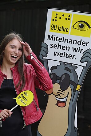 Eine junge Frau mit dunklen Haaren vor der Pappfigur AUGust