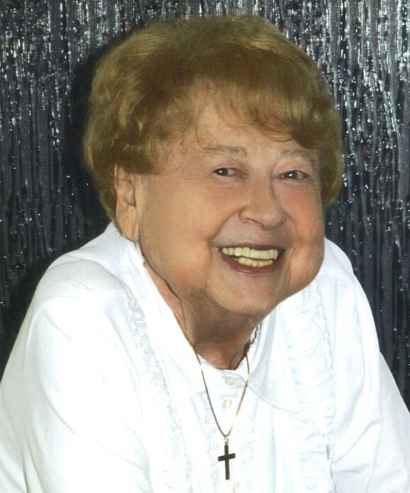 Waltraude Köckeis kam durch ihre eigene Sehbehinderung mit der Hilfsgemeinschaft in Kontakt. Foto: privat. ältere Frau mit weißem Shirt und dunkelblonden Haaren lächelt in die Kamera, Hintergrund in silber