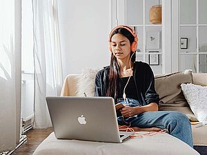 Eine junge Frau sitzt vor einem Laptop. Sie hat Kopfhörer aufgesetzt.