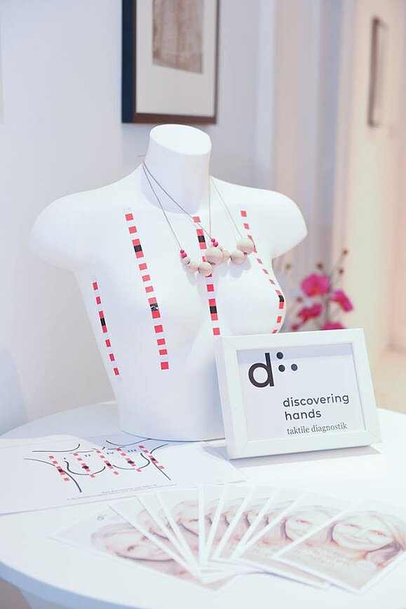 Standardisierte Methode mithilfe patentierter Spezialklebestreifen, Copyright: discovering hands. Weiße Büste mit Spezialklebestreifen und Kette mit Holzperlen.