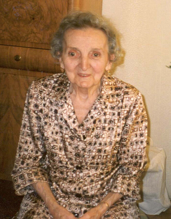 Maria Gumpinger Eine ältere Dame mit Dauerwelle sitzt lächelnd auf einem Sessel