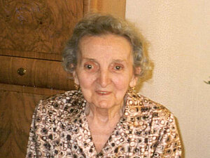 Maria Gumpinger Eine ältere Dame mit Dauerwelle sitzt lächelnd auf einem Sessel