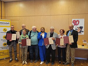 Feierliche Übergabe der Ehrungen Mehrere Personen stehen nebeninander und halten eine Urkunde in der Hand. In der Mitte steht eine Frau die moderiert und der Vorstandsvorsitzende Fürst