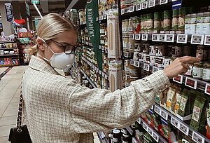 Eine Frau mit Mund-Nasen-Schutz steht vor einem Supermarktregal.
