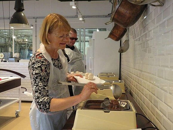 Schwedenbomben, Marke „Eigenbau“ Dame gießt flüssige Schokolade mit einem Schöpfer über den Teig einer Schwedenbombe.