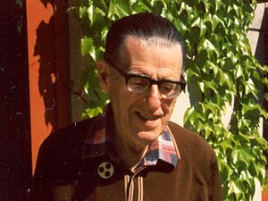 Willibald Mang Älterer Herr mit Brille und Anstecknadel vor einer mit wildem Wein bewachsenen Hauswand