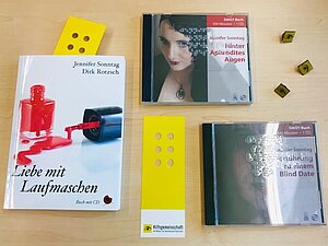 Buch "Liebe mit Laufmaschen", CD "Hinter Aphrodites Augen" und CD "Verführung zu einem Blind Date" liegen mit Button und Lesezeichen auf einem Tisch.