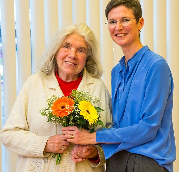 Eva Fichte mit Mitarbeiterin Alexandra Kleinheinz (c) Franz Pflügl. Ältere Frau mit weißen Haaren hält gemeinsam mit jüngerer Frau mit kurzen Haaren und Brille einen Blumenstrauß, beide lächeln in die Kamera