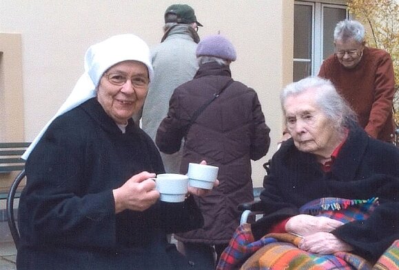 Schwester Consulate mit Frau Fiala Nonne mit Teetasse in der Hand und ältere Dame mit Decke schauen in die Kamera