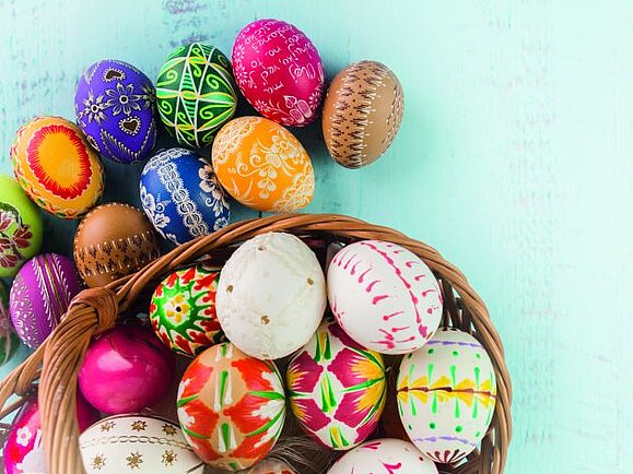 Viele buntbemalte Ostereier liegen in und neben einem Korb auf einem türkisfarbenem Hintergrund.