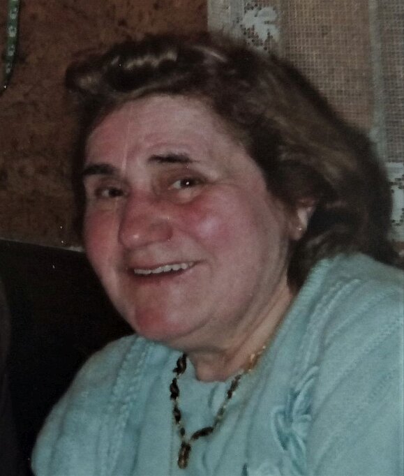 anna_starycha_testamentsspenderin_hilfsgemeinschaft ältere Frau mit blauem Pullover, braunen schulterlangen Haaren und roten Backen lächelt in die Kamera