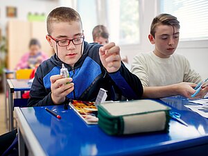 Bub mit Behinderung bastelt in der Schule mit anderen Kindern.