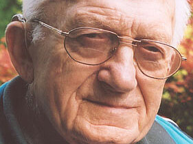 Otto Salzborn Ein älterer Herr mit Brille lächelt freundlich in die Kamera, hinter ihm grüne Bäume